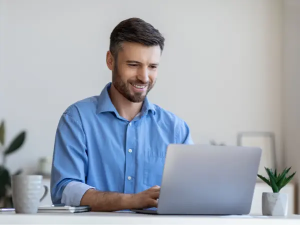 Sinipaitainen mies istuu läppärin edessä